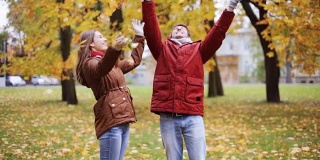 快乐的年轻夫妇在公园里扔秋叶