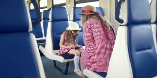 小女孩在火车上用智能手机，坐在她妈妈的前面