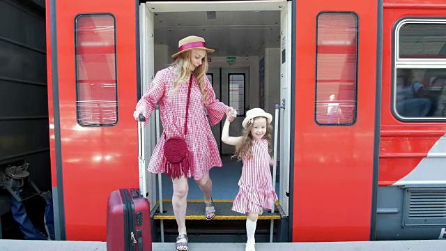 一位年轻的妇女提着手提箱和她的小女儿离开了火车车厢