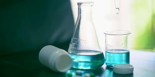 明亮的慢动作化学溶液滴在烧杯上，用于测试桌上药物的化学反应