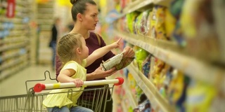 母亲和女儿在超市购物。他们在买早餐片。坐在超市购物车里的女儿