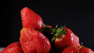 在黑色的背景上，一个草莓落在一把浆果上视频素材模板下载