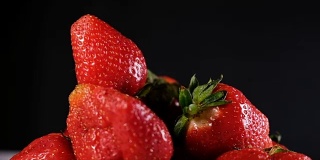 在黑色的背景上，一个草莓落在一把浆果上