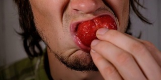 残忍的男人正在吃多汁的草莓特写。一个恶心的饥肠辘辘的家伙恶心地嚼着一颗成熟的大浆果