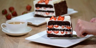 把一块带新鲜草莓的巧克力蛋糕放在盘子里。
