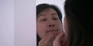 一名泰国妇女正在镜子旁挤她脸上和嘴上的痘痘