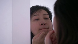 一名泰国妇女正在镜子旁挤她脸上和嘴上的痘痘视频素材模板下载