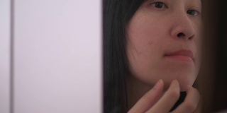亚洲美丽的女人正在挤压周围的痘痘在她的脸和嘴巴旁边的镜子