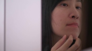 亚洲美丽的女人正在挤压周围的痘痘在她的脸和嘴巴旁边的镜子视频素材模板下载