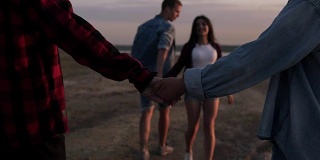 幸福的男人和女人夫妇散步和手牵手在一个荒凉的海滩傍晚黄昏的天空。两对夫妇在户外散步。青年文化。快乐的年轻人