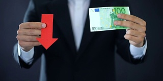 商人展示欧元纸币和红色箭头标志，货币下跌，危机