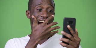 年轻快乐的非洲男子在使用电话时看起来很震惊