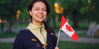 慢动作肖像迷人的女孩加拿大体育迷拿着加拿大国旗，看着镜头微笑。人与国的观念。