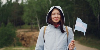 女性世界旅行者的慢动作肖像举着阿根廷国旗在风中飘扬，微笑着看着相机。背景是美丽的绿色森林。