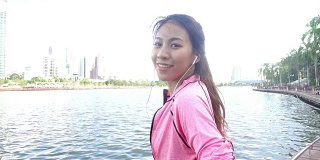 慢动作——穿着健身服的亚洲美女正在用智能手表听音乐，在公园跑步后打电话。有吸引力的健康女性慢跑。