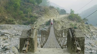 两名背包客在尼泊尔的一座悬空金属桥上行走。视频素材模板下载