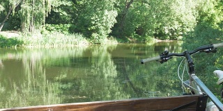 一个人骑着自行车，在公园里夏天休息。他坐在池塘边的长椅上。