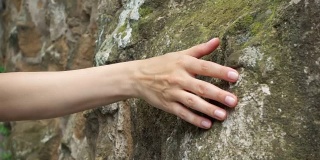 一个女人用手在古老的石墙上慢动作画。女性的手触摸岩石的粗糙表面