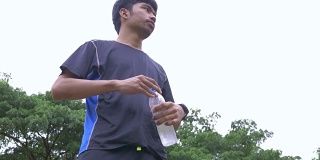 跑步者在户外慢跑时饮用瓶装水。亚洲人训练马拉松赛跑