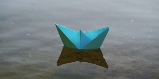 蓝色的纸船在浪漫的日落水上航行。