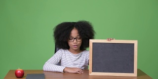 年轻可爱的非洲女孩与非洲发式显示黑板而坐