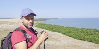 用双筒望远镜观察野生动物的旅行者。男人们在度假中观赏自然景观。一个背包旅行者正在用双筒望远镜看大海，看美丽的风景。山。海滩。