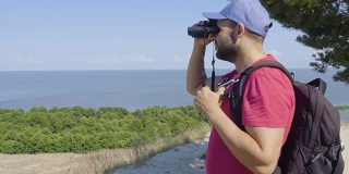 用双筒望远镜观察野生动物的旅行者。男人们在度假中观赏自然景观。一个背包旅行者正在用双筒望远镜看大海，看美丽的风景。山。海滩。