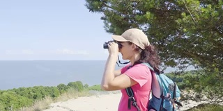 用双筒望远镜观察野生动物的旅行者。女人在度假看自然景观。一个背包旅行者正在用双筒望远镜看大海，看美丽的风景。山。海滩。