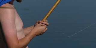 一个人拿着钓竿在湖边钓鱼。在钓鱼的时候，男人的手在鱼竿钩上戴一个鱼饵。