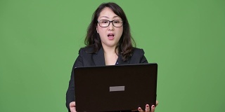 成熟美丽的亚洲商人在绿色背景下使用笔记本电脑