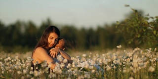 一个年轻快乐的母亲和孩子在一个花田在日落的慢镜头。