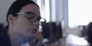 紧张的工作，疲惫的年轻女子戴着眼镜梦想在办公室的工作场所近距离