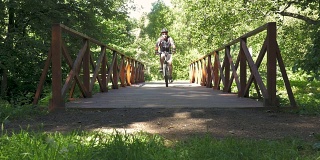 公园里，一个男人骑着自行车过桥。慢动作