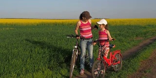 一个妇女和一个孩子在乡下骑自行车。本质上是一个体育家庭。妈妈和女儿骑着自行车在田野里