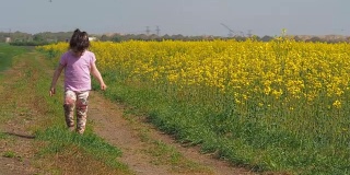 小女孩在草地上跑。那孩子在乡间小路上奔跑。一个快乐的孩子在黄色的花丛中奔跑。油菜籽领域