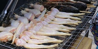 烹饪商人在炉子上用火烤鲜鸡翅，在火上冒烟。街上的泰国菜，视频片段1920x2080。手工烹饪的概念。
