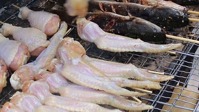 烹饪商人在炉子上用火烤鲜鸡翅，在火上冒烟。街上的泰国菜，视频片段1920x2080。手工烹饪的概念。