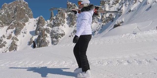 在高山滑雪胜地，一名滑雪者肩上扛着下坡滑雪板前进