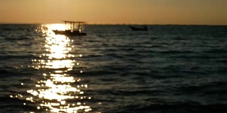 4K镜头抽象模糊背景。日落或日出时海面上小船的剪影，夏日热带海滩上美丽的阳光反射在水面上