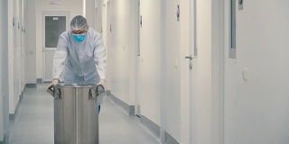 穿着防护服的工人推着桶穿过实验室走廊