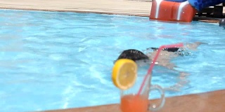 一个阳光明媚的小男孩在游泳池喝着鸡尾酒