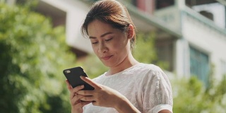 亚洲美女正在使用智能手机上网和聊天的朋友在花园里