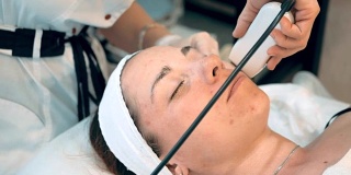 年轻女子面部皮肤清洁程序。美容师使用特殊的医疗设备配合面部工作，病人闭着眼睛躺着。美容、水疗和美容