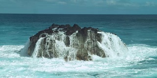 慢动作:泛着泡沫的海水顺着翠绿的海洋中的一块黑色大岩石流下去。
