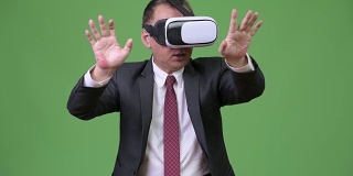 成熟的日本商人在绿色背景下使用虚拟现实头盔