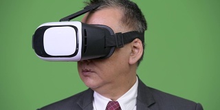 成熟的日本商人在绿色背景下使用虚拟现实头盔