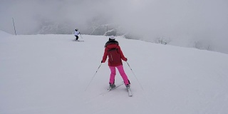 两名运动女滑雪者在冬季大雾中下山滑雪
