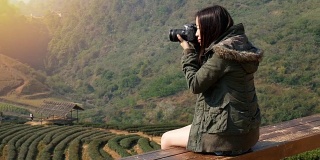 快乐的亚洲女游客在日出时间用数码相机拍摄亚洲茶园美丽自然的4K镜头。旅游度假概念
