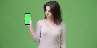 年轻美丽的女人在绿色背景下展示手机