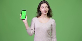 年轻美丽的女人思考，而显示手机对绿色的背景